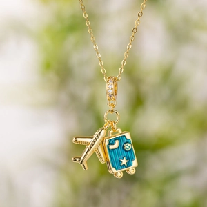 Gold airplane and blue suitcase travel necklace with sparkling paved stones on lush green
