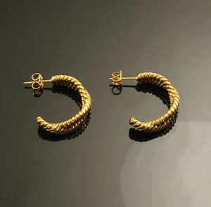 Close-up of gold-plated geometric C-shaped twisted metal earrings on reflective surface