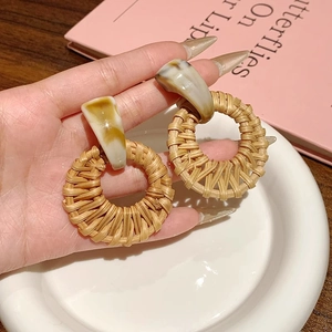 Détail de boucles d'oreilles pendantes en rotin naturel présentées sur un plat blanc