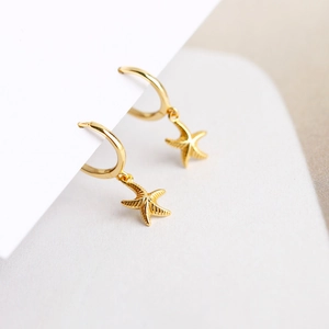 Detail view of gold-plated starfish charms dangling on small sterling silver hoop earrings
