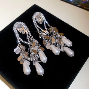 Detailed macro view of gold-plated silver needle earrings with teardrop pearls and crystals