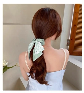 Close-up of a mint green floral bow scrunchie with streamers styled on a low ponytail