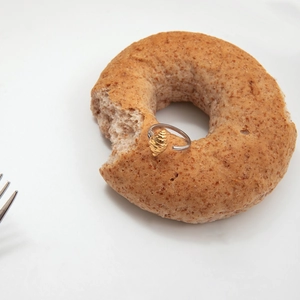 Vue macro d'une bague réglable bicolore or et argent en forme de croissant sur un bagel