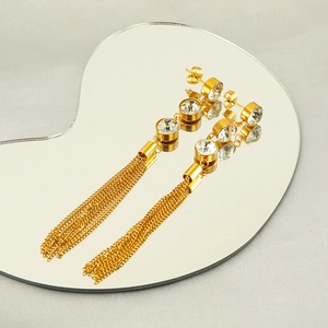 Vue macro de boucles d'oreilles longues dorées à pompons avec zircons sur miroir