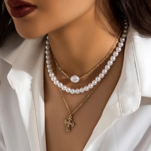 Close-up of triple-layered gold necklaces with cross pendant and pearl on white shirt