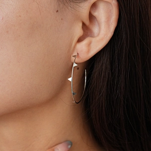 Detail of silver geometric hoop earring with metal rivets worn by a model