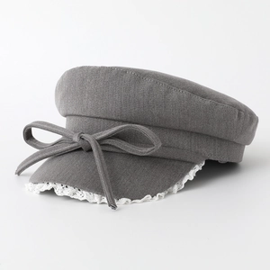 Dark grey flat top newsboy hat with bow tie and white lace trim detail in studio lighting