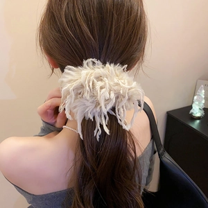 Détail d'un chouchou élégant en plumes beige porté sur une coiffure en queue de cheval