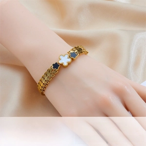 Detail of gold clover bracelet featuring black and white charms on satin background