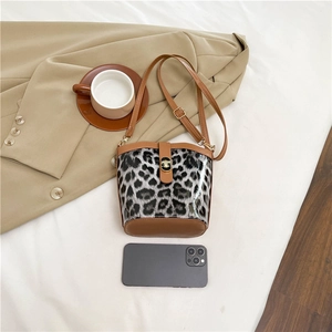 Leopard print bucket bag with brown PU leather trim and metal clasp on beige background