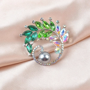 Detailed macro view of the luxury green crystal leaf brooch with grey pearl on silk