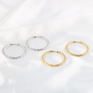 Minimalist textured hoop earrings in gold and silver finish on white silk background