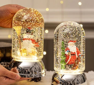 Close-up of a hand holding a glowing Christmas snow globe with Santa and snowman motifs