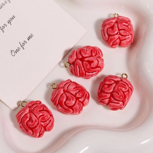 Close-up of five red resin brain-shaped charms with gold loops on a pink plate
