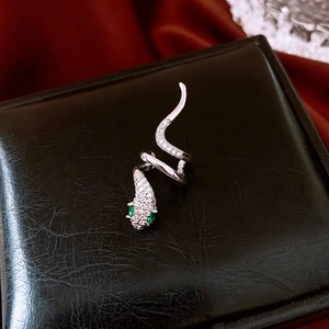 Macro shot of silver snake ring with white zircons and green eyes on black leather box