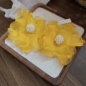 Gros plan de boucles d'oreilles fleurs en tissu jaune avec perles sur plateau en bois.