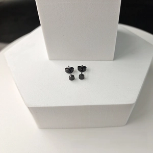 Macro shot of a pair of black round stainless steel stud earrings on a white platform