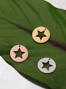 Three hollow star pendant charms in gold, silver, and rose gold finishes on a leaf