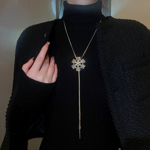 Détail du collier flocon de neige doré avec perles et longs pompons sur un pull