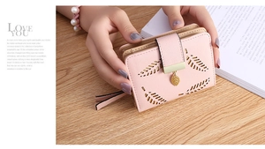 Pink short wallet with leaf cut-out design and gold leaf pendant held against a book