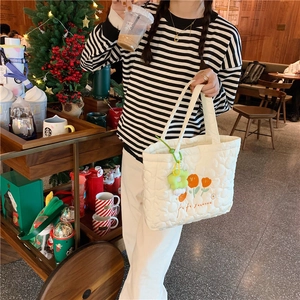 Detail of white quilted tote bag featuring orange tulip embroidery and green flower charm