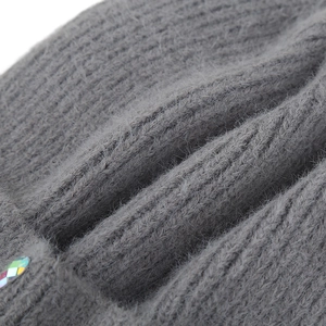 Détail macro du bonnet en maille grise montrant la texture douce et les strass colorés
