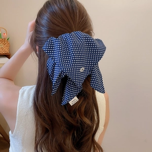 Deep blue polka dot bow hair scrunchie shown on a woman back hairstyle in natural light