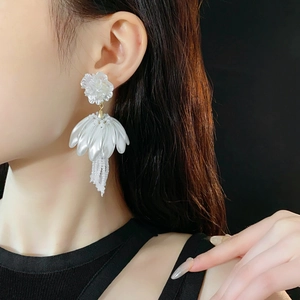 Detail of white petal earrings with beads fringe on a model over black background