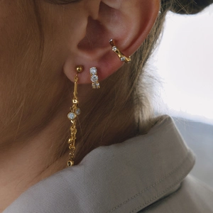 Close-up of 18K gold earrings set with sparkling zircon tassels and wave ear cuff
