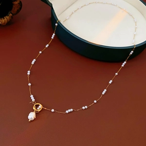 Pendentif perle baroque sur chaîne dorée en acier inoxydable sur fond rouge foncé