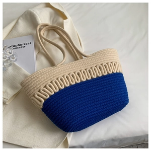 Close-up of a blue and beige woven tote bag with knotted handles on white sheets