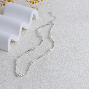 Detail of silver beaded freshwater pearl necklace with lobster clasp on white surface