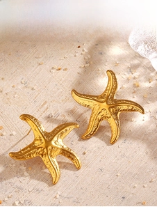 Macro shot of gold starfish earrings with textured hammered finish on sand background