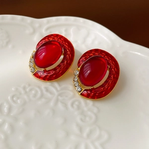 Macro detail of vintage red oval earrings with gold trim and crystal accents on ceramic