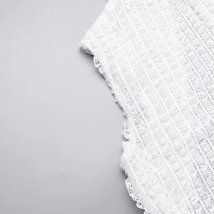 Detail shot of white textured fabric with 3D weaving and lace edges on a minimalist dress