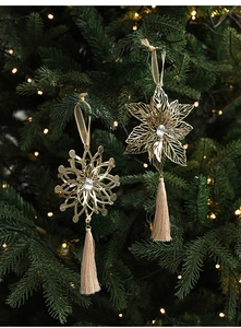 Detail of golden metal snowflake ornament with long tassels hanging on a Christmas tree