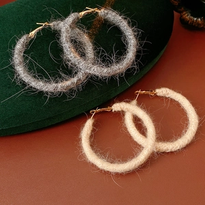 Dettaglio di orecchini a cerchio in lana grigia e beige con chiusura dorata