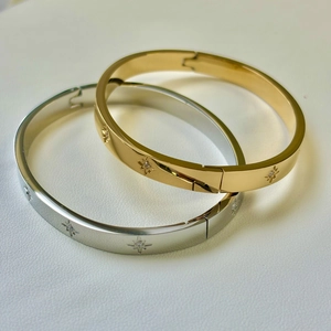 Macro detail of gold and silver star engraved stainless steel bangles on white leather
