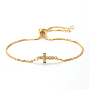 Detailed close-up of a golden cross bracelet with cubic zirconia and adjustable chain