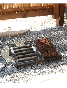 Macro shot of vintage cast iron boot scraper with stiff bristles on a garden gravel path