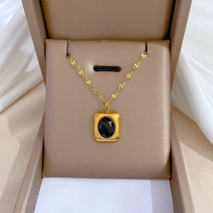Macro detail of gold vintage rectangular pendant with black oval gemstone on floral chain