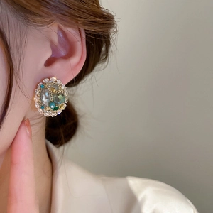 Detail of vintage round gold earrings with grey-green gem and white zircon accents