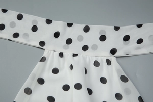 Detailed close-up of white chiffon fabric with black polka dots and pleated neckline