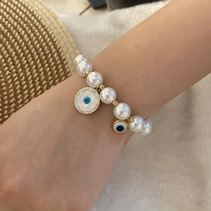 Elegant white pearl beaded bracelet with gold accents and evil eye charms on wrist