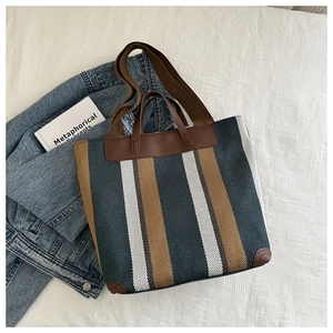 Flat lay of striped canvas tote bag with brown leather handles and a long shoulder strap