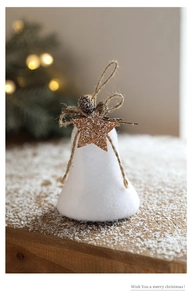 Close-up of white plush bell ornament with pine cone and wooden star on a snowy surface