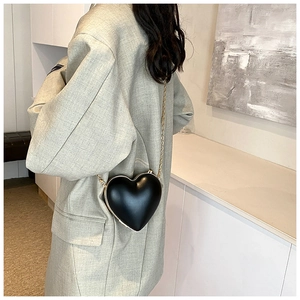 Detail of a chic heart-shaped black crossbody bag with a premium golden chain strap