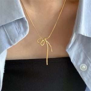 Close-up of golden bow-knot pendant necklace worn over a light blue shirt