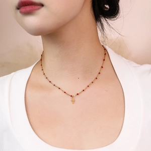 Close-up of gold chain necklace with red beads and a small cross pendant on a model
