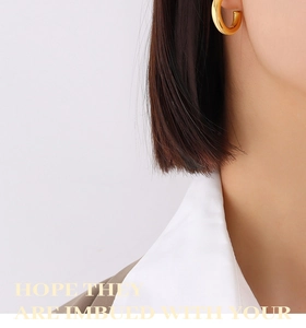 Detailed view of polished 18K gold C-shaped hoop earrings worn on a model's ear lobe